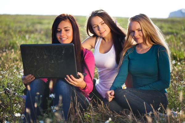Tři krásná mladá žena s notebookem sedět v poli o — Stock fotografie