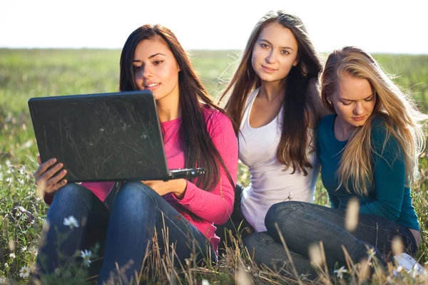 Three young beautiful woman with a laptop sitting in the field o — Stock Photo, Image