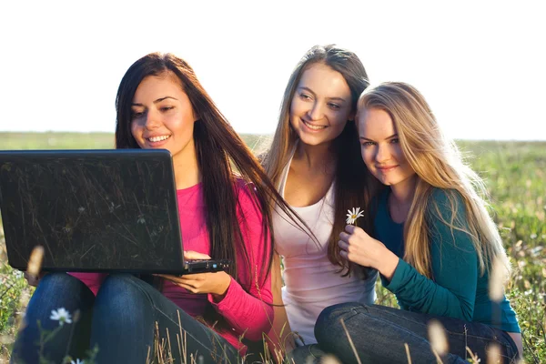 Three young beautiful woman with a laptop sitting in the field o — Stock Photo, Image