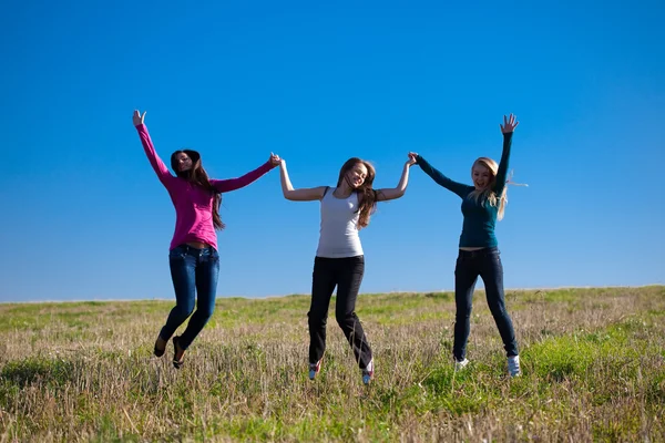 Tre unga vackra kvinnan hoppa i fältet mot s — Stockfoto