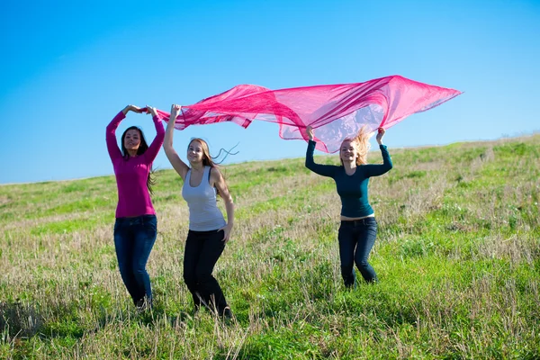 Tre giovani bella donna che salta con tessuto nel campo a — Foto Stock