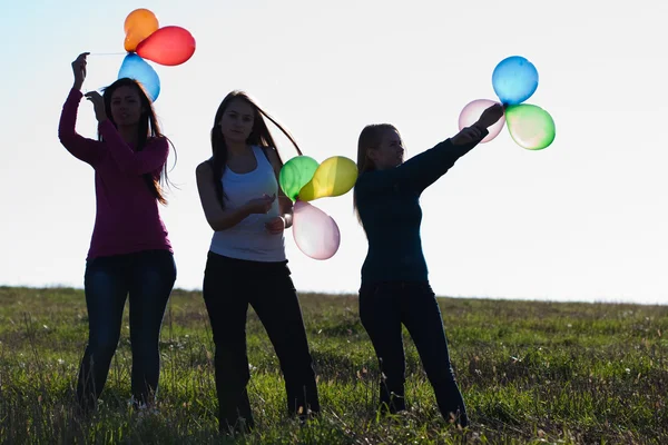 Три молодих красивих жінки з повітряними кулями в поле проти — стокове фото