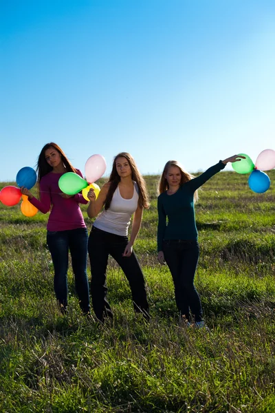 Three young beautiful woman with balloons into the field against — Stock Photo, Image