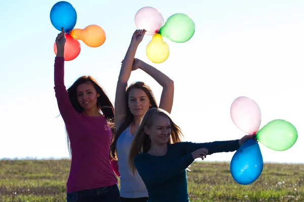 Tres mujeres hermosas jóvenes con globos en el campo contra — Foto de Stock