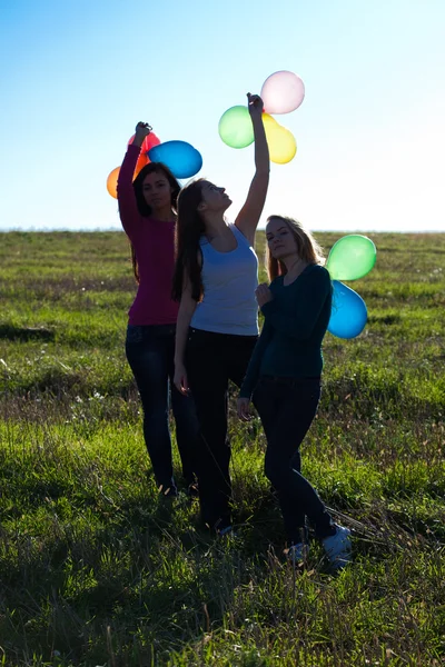 Три молодих красивих жінки з повітряними кулями в поле проти — стокове фото