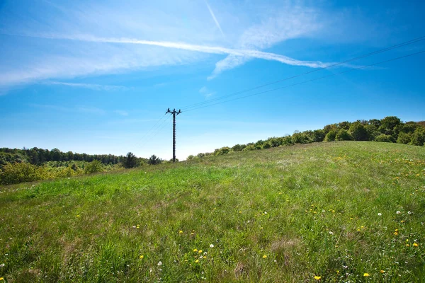 Prado e linha de energia contra o céu azul — Fotografia de Stock