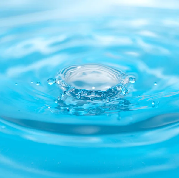 Goccia d'acqua e spruzzi su uno sfondo blu — Foto Stock