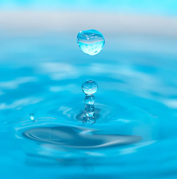 Water drop and splash on a blue background — Stock Photo, Image