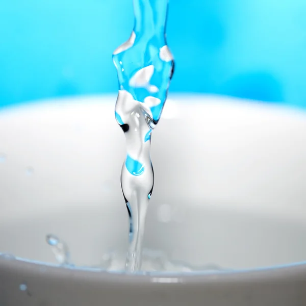 Spruzzi d'acqua in una tazza su uno sfondo blu — Foto Stock