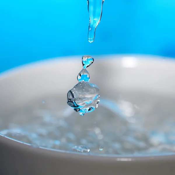 Water splash in een cup op een blauwe achtergrond — Stockfoto