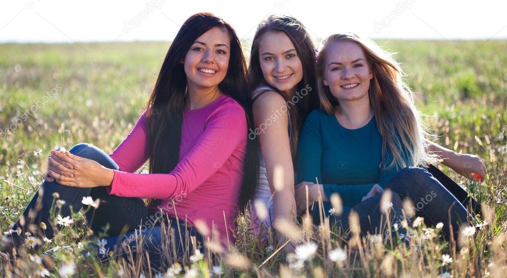 Three young beautiful woman sitting in a field on the sky backg