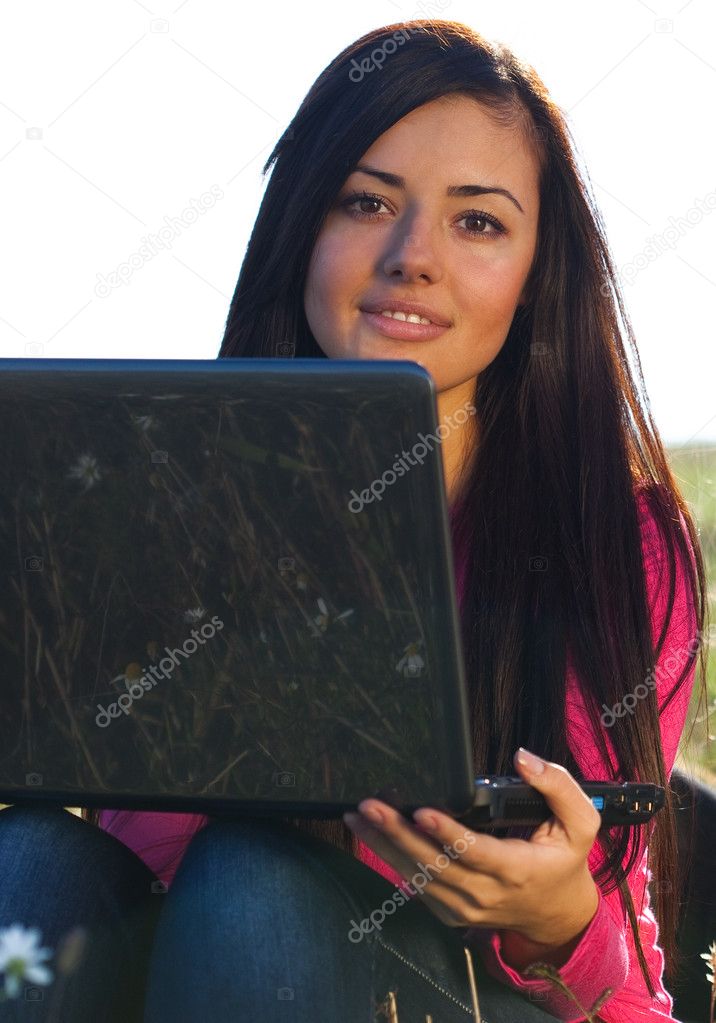Young beautiful woman with a laptop sitting in the field on sky