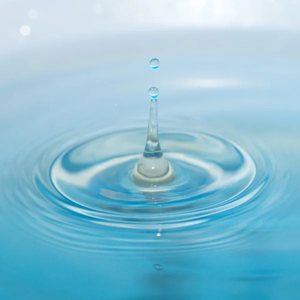 Water drop and splash on a blue background — Stock Photo, Image