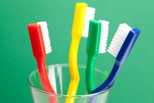 Bir bardak yeşil bir arka plan üzerinde Renkli diş fırçası — Stok fotoğraf