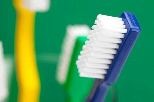 Bir bardak yeşil bir arka plan üzerinde Renkli diş fırçası — Stok fotoğraf