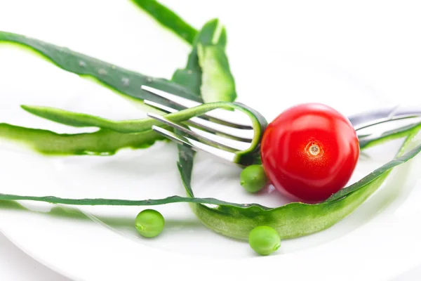 Tomaten, Erbsen, Gabel und Gurkenschale auf einem Teller isoliert auf weiß — Stockfoto