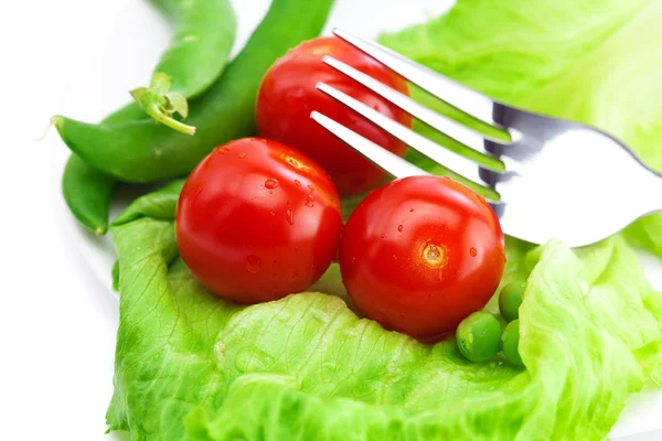 Tomato,peas and lettuce with a fork on a plate isolated on white — Stock Photo, Image