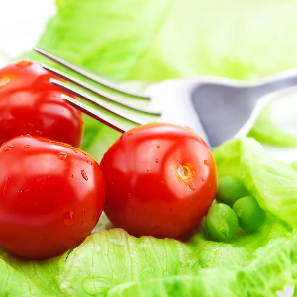 Tomate, guisantes y lechuga con un tenedor en un plato aislado en blanco — Foto de Stock