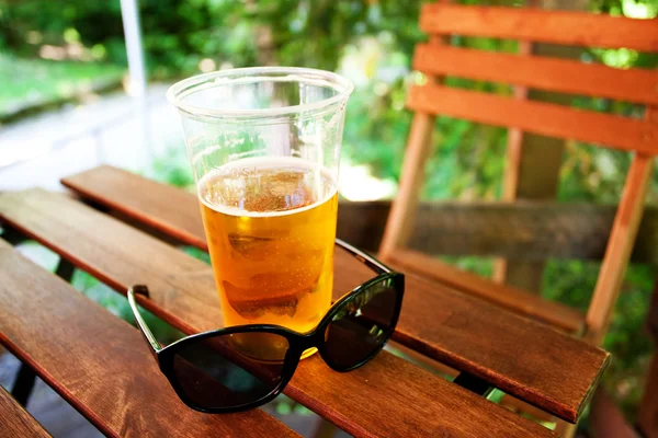 Piwo i okulary przeciwsłoneczne, stojąc na drewnianym stołem — Zdjęcie stockowe