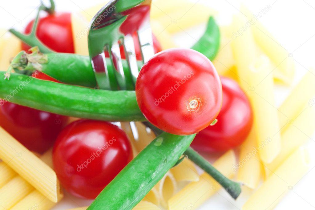 Tomatoes, peas, pasta and fork on a plate isolated on white