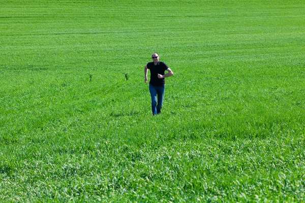 Jovem em óculos de sol correndo em campo verde — Fotografia de Stock