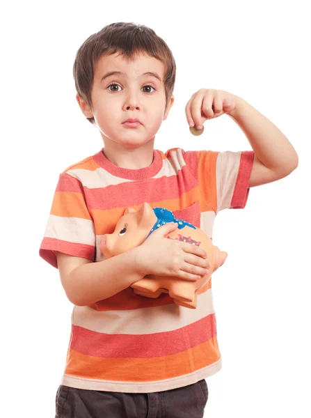 Грустный маленький мальчик кладет монетку в копилку — стоковое фото