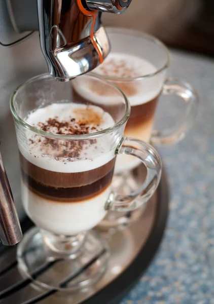 Due bicchieri fileed con cappuccino in macchina da caffè — Foto Stock
