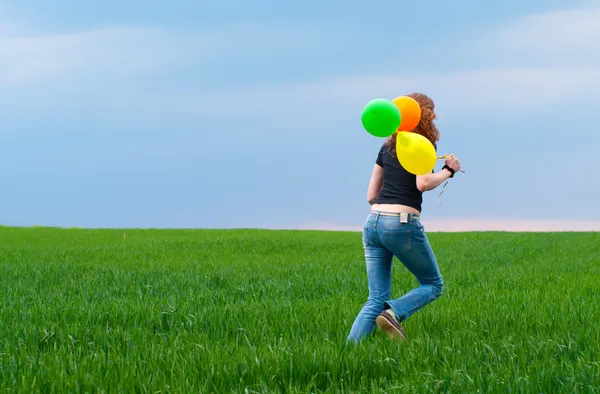 Donna in fuga con palloncini gialli sul campo verde — Foto Stock
