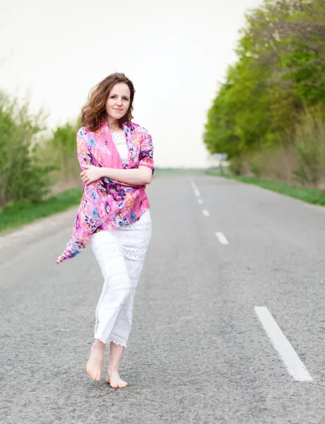 Woman in colorful shawl walking the empty highway — Stock Photo, Image