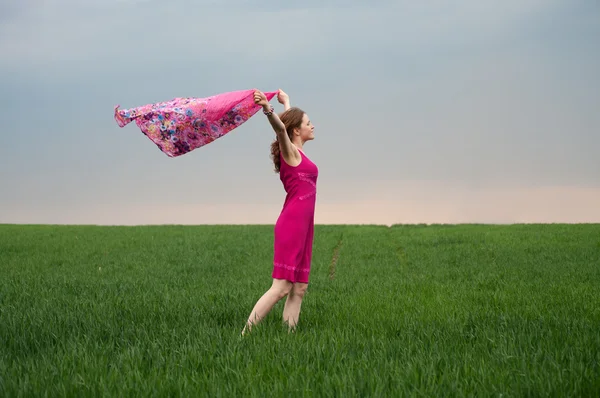 Meisje in roze jurk in groene veld op de wind — Stockfoto