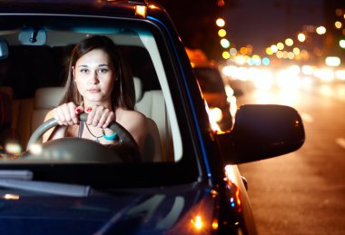 Young woman driving car in the night city clipart