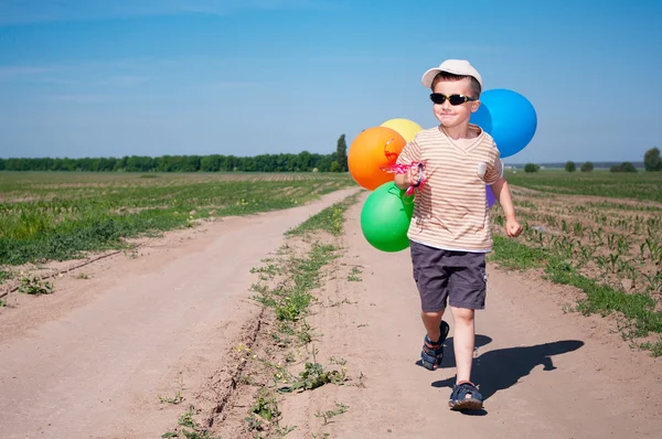 Liten pojke med färgglada ballonger går landsvägen — 图库照片