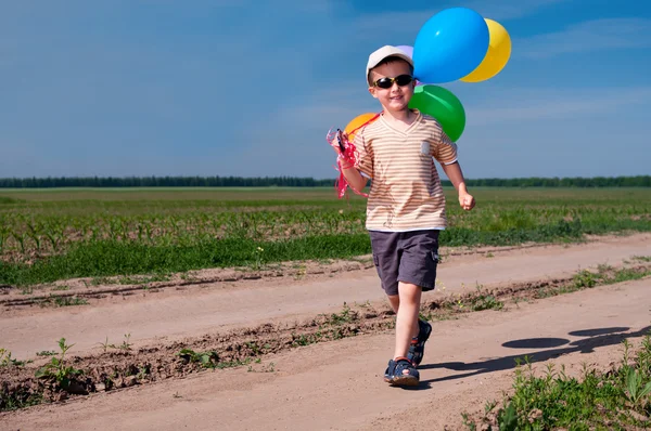 Мальчик с разноцветными воздушными шарами идет по проселочной дороге — стоковое фото