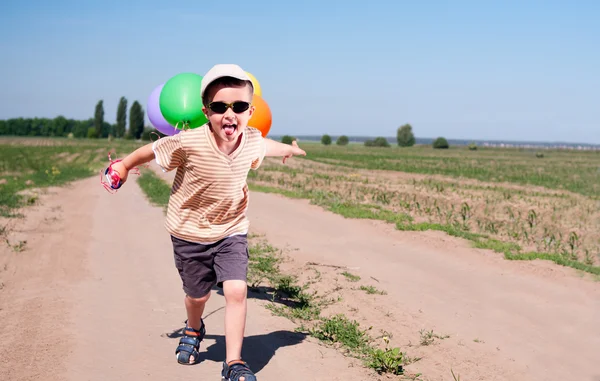 Little boy with colorful balloons running the country road — Stock Photo, Image