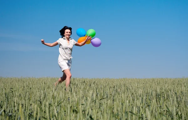 Mulher correndo no campo de trigo com balões coloridos — Fotografia de Stock