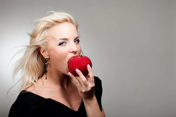 Блондинка, кусающая красное яблоко — стоковое фото