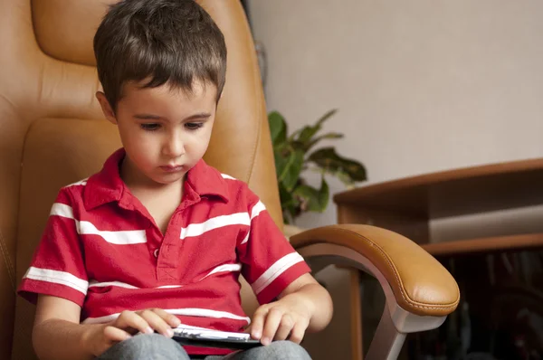 Liten pojke spela smartphone spel i läder stol — Stockfoto