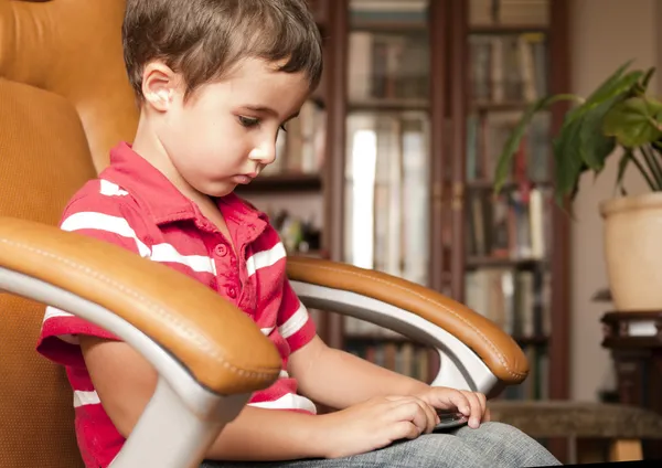 Petit garçon jouer jeu smartphone dans une chaise en cuir — Photo