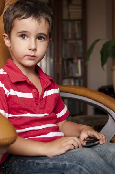 Lille dreng spille smartphone spil i læder stol - Stock-foto