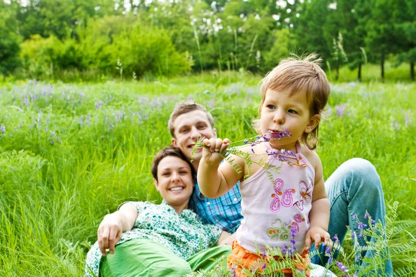Toddler eating flower, smiling parents in back — Stock Photo, Image