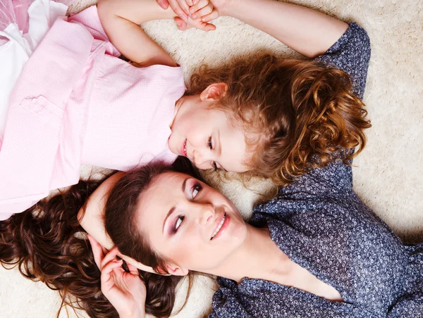 Klein meisje en moeder liggen op het tapijt — Stockfoto