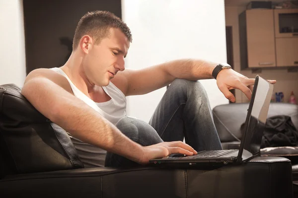 Lachende jonge man aan het werk op laptop thuis — Stockfoto