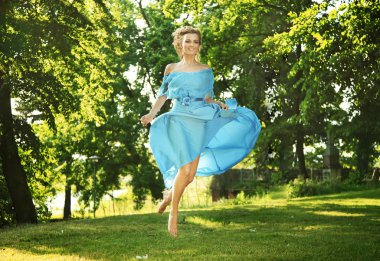 Young charming laughing woman in beautiful dress jumps on meadow