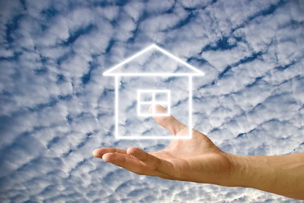 Hus ikon i handen med grumlig himmel bakgrund — Stockfoto