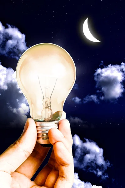 A kéz meleg lámpa izzó ragyogjon a fény, a Hold és a háttérégbolt segítségével — Stock Fotó