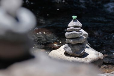 Cairn with green stone by the stream clipart