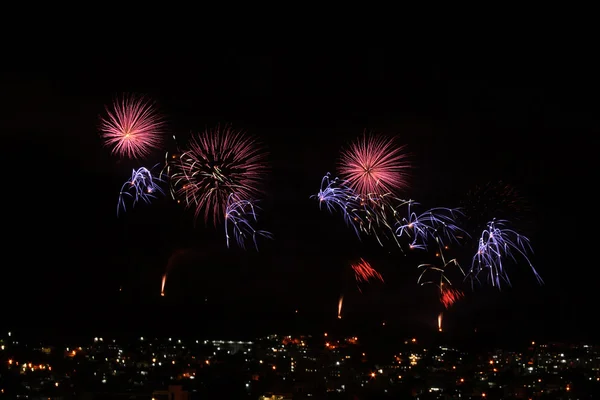 Fireworks displaying pink and blue over town — Stock Photo, Image