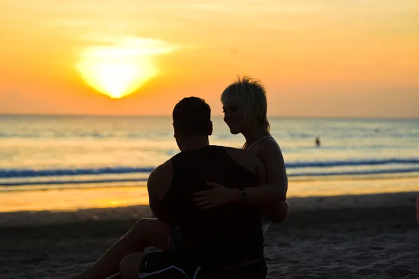 Two young lovers sitting on a beach and looking to each other — Stock Photo, Image