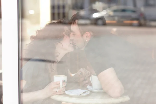 Ung man kysser vacker flicka på café. reflektion i glas — Stockfoto