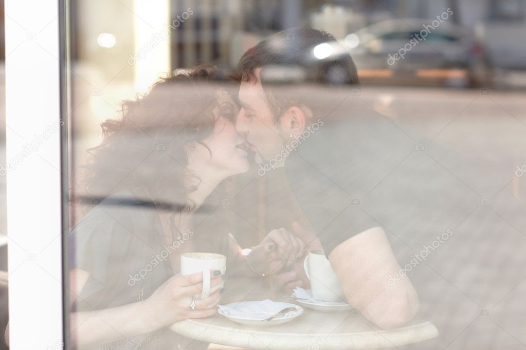 Young man kisses beautiful girl on cafe. reflection in the glass